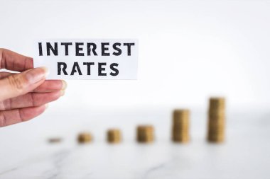 Interest Rates text with growing stacks of coins representing increasingly expensive loans and mortgages, concept of global economy struggling after the covid-19 pandemic