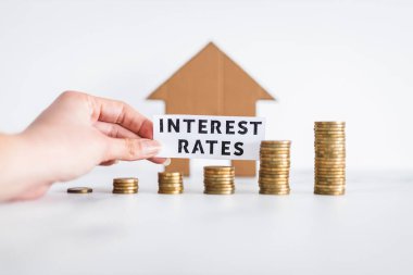 Interest Rates text with growing stacks of coins representing increasingly expensive loans and mortgages with cardboard house in the background, concept of global economy after the pandemic