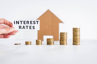 Interest Rates text with growing stacks of coins representing increasingly expensive loans and mortgages with cardboard house in the background, concept of global economy after the pandemic