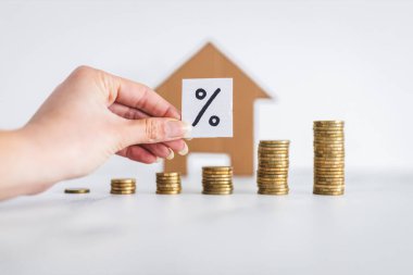 interest rates for loans and mortgages going up conceptual image, percentage symbol with growing stacks of coins representing increasingly expensive cost of financing in front of cardboard house