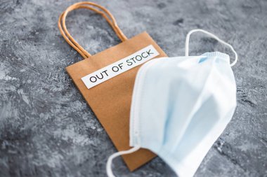 Out of Stock text on top of shopping bag with surgical mask, concept of supply chain shortages and delays after the covid-19 global pandemic