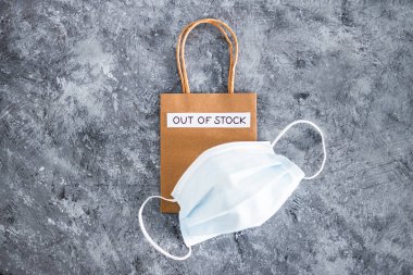 Out of Stock text on top of shopping bag with surgical mask, concept of supply chain shortages and delays after the covid-19 global pandemic