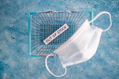 out of stock text inside of empty shopping basket with surgical mask, concept of supply chain shortages and delays after the covid-19 global pandemic