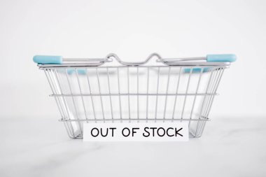 out of stock text in front of empty shopping basket on white background, concept of supply chain shortages and delays after the covid-19 global pandemic