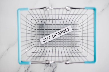 out of stock text in front of empty shopping basket on white background, concept of supply chain shortages and delays after the covid-19 global pandemic