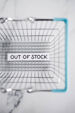 out of stock text in front of empty shopping basket on white background, concept of supply chain shortages and delays after the covid-19 global pandemic