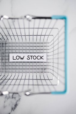 Low stock text in front of empty shopping basket on white background, concept of supply chain shortages and delays after the covid-19 global pandemic
