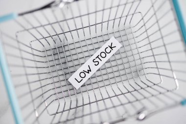 Low stock text in front of empty shopping basket on white background, concept of supply chain shortages and delays after the covid-19 global pandemic