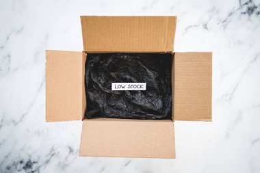 Low stock text inside of empty delivery parcel with black padding on white background, concept of supply chain shortages and delays after the covid-19 global pandemic