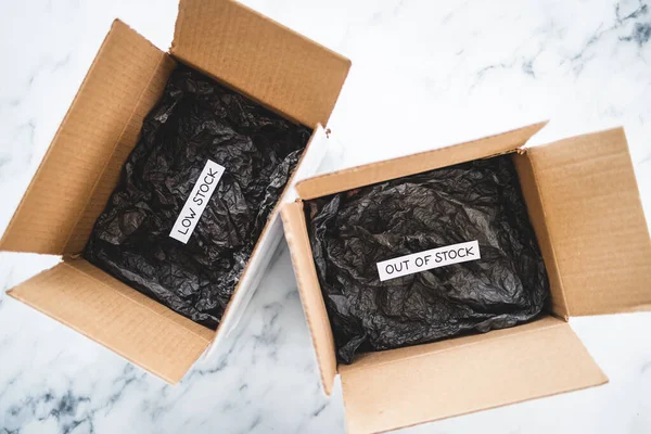 Low stock and out of stock texts inside of empty delivery parcels with black padding on white background, concept of supply chain shortages and delays after the covid-19 global pandemic