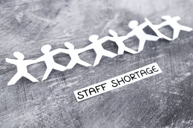 staff shortages and business struggling after the pandemic conceptual image, peper people chain with text on gray background
