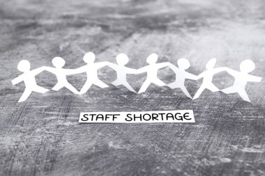 staff shortages and business struggling after the pandemic conceptual image, peper people chain with text on gray background