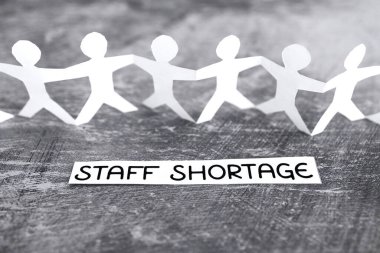 staff shortages and business struggling after the pandemic conceptual image, peper people chain with text on gray background