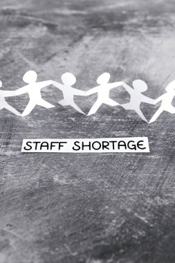 staff shortages and business struggling after the pandemic conceptual image, peper people chain with text on gray background