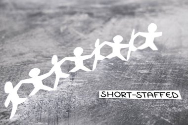 staff shortages and business struggling after the pandemic conceptual image, peper people chain with Short-staffed text on gray background