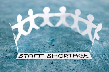 staff shortages and business struggling after the pandemic conceptual image, peper people chain with text on blue background