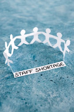 staff shortages and business struggling after the pandemic conceptual image, peper people chain with text on blue background
