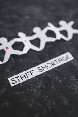 staff shortages and business struggling after the pandemic conceptual image, paper people chain with some workers crossed out and Covid Staff Shortage text on black background