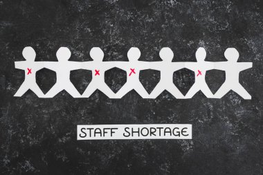 staff shortages and business struggling after the pandemic conceptual image, paper people chain with some workers crossed out and Covid Staff Shortage text on black background