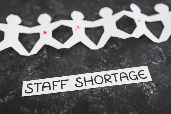 staff shortages and business struggling after the pandemic conceptual image, paper people chain with some workers crossed out and Covid Staff Shortage text on black background
