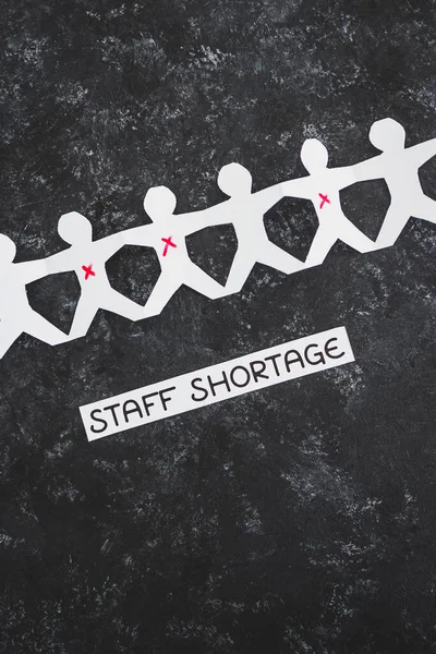 staff shortages and business struggling after the pandemic conceptual image, paper people chain with some workers crossed out and Covid Staff Shortage text on black background
