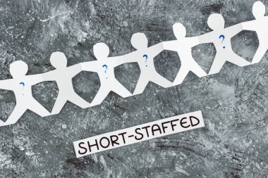 staff shortages and business struggling after the pandemic conceptual image, paper people chain with question marks on some workers and Short-staffed text on black background