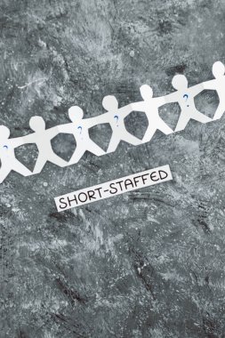 staff shortages and business struggling after the pandemic conceptual image, paper people chain with question marks on some workers and Short-staffed text on black background