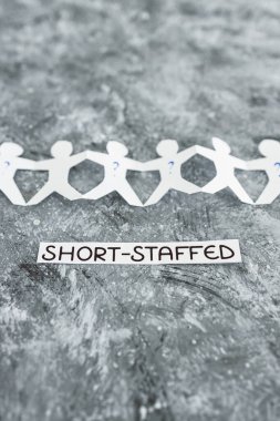 staff shortages and business struggling after the pandemic conceptual image, paper people chain with question marks on some workers and Short-staffed text on black background