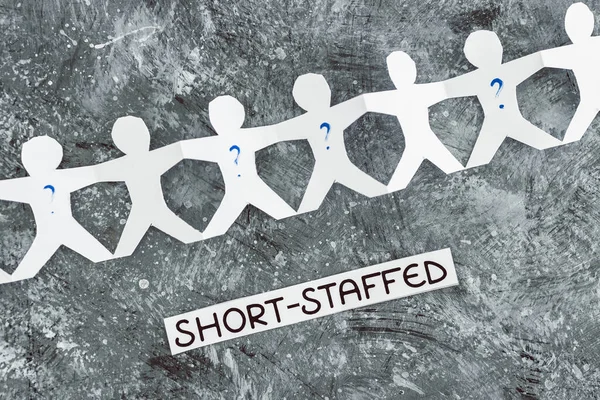 staff shortages and business struggling after the pandemic conceptual image, paper people chain with question marks on some workers and Short-staffed text on black background
