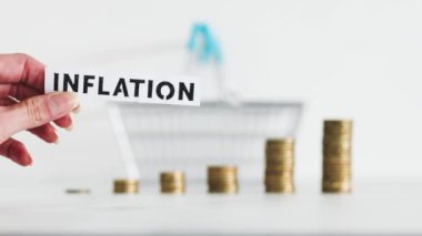 inflation text in front of shopping basket and growing stacks of coins representing increasingly expensive prices, concept of global economy struggling after the covid-19 pandemic