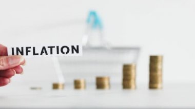 inflation text in front of shopping basket and growing stacks of coins representing increasingly expensive prices, concept of global economy struggling after the covid-19 pandemic