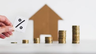 interest rates for loans and mortgages going up conceptual image, percentage symbol with growing stacks of coins representing increasingly expensive cost of financing in front of cardboard house