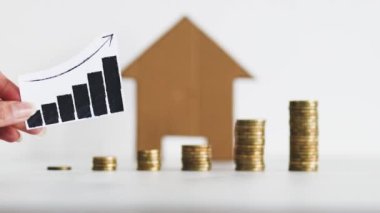 interest rates for loans and real estate prices going up conceptual image, graph with upward trend with growing stacks of coins in front of cardboard house