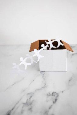 Think outside the box concept with paper people chain getting out of a white box on white marble	with minimalistic composition