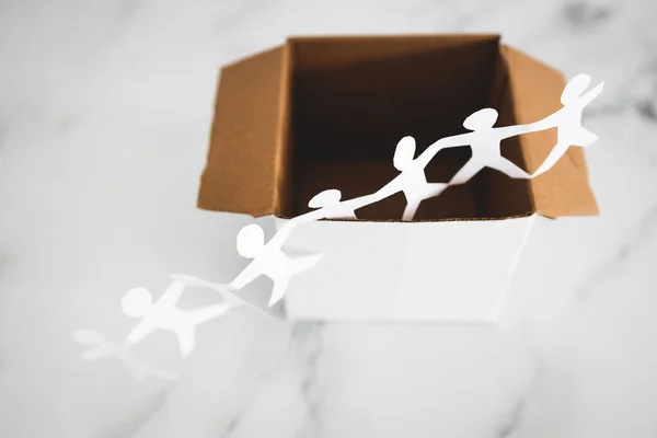 Think outside the box concept with paper people chain getting out of a white box on white marble	with minimalistic composition