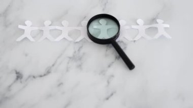 staff shortages and hiring personnel conceptual image, paper people chain with magnifying glass analysing them
