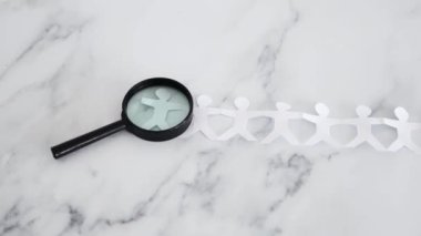 staff shortages and hiring personnel conceptual image, paper people chain with magnifying glass analysing them