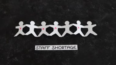 staff shortages and business struggling after the pandemic conceptual image, paper people chain with some workers crossed out and Covid Staff Shortage text on black background