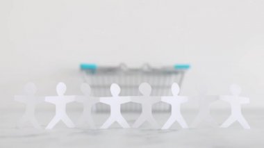 consumerism or inflation conceptual image, paper people chain in front of oversize empty shopping basket