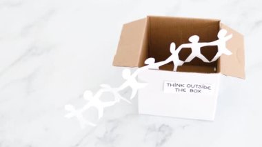 Think outside the box concept with paper people chain getting out of a white box with text on white marblewith minimalistic composition