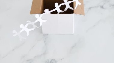 Think outside the box concept with paper people chain getting out of a white box on white marblewith minimalistic composition