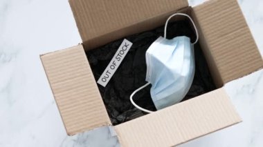 Out of stock text inside of empty delivery parcel with surgical mask on white background, concept of supply chain shortages and delays after the covid-19 global pandemic