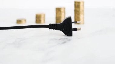 Elektrik maliyetleri kavramsal görüntüde yükseliyor, arka planda artan madeni para yığınlarıyla fiş takılıyor ve fiyatlar yükseliyor.