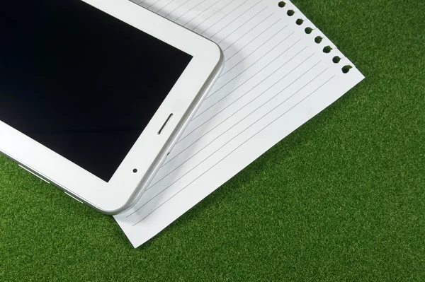Yeşil çimenlerin üzerinde Tablet ve satır boş kağıtlar.