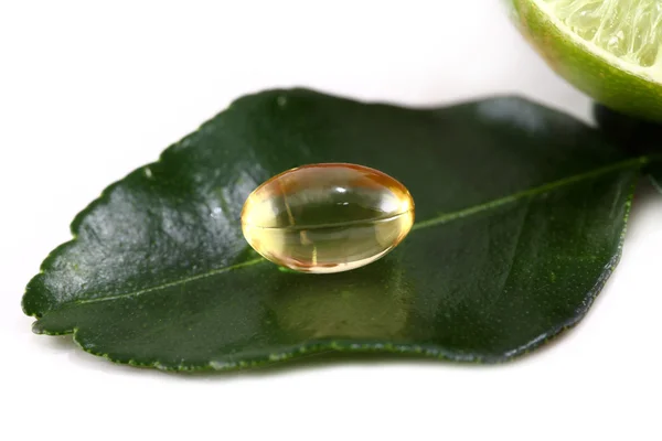 Pílulas de óleo de ervas medicinais com planta verde no fundo branco — Fotografia de Stock