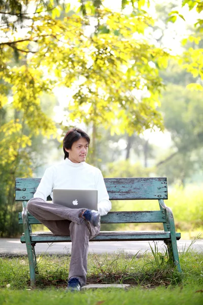 Un jeune homme beau utilisant un ordinateur portable assis sur un banc regardant dans — Photo