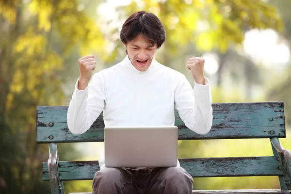 Un jeune bel homme asiatique en utilisant un ordinateur portable assis sur un banc dans un — Photo