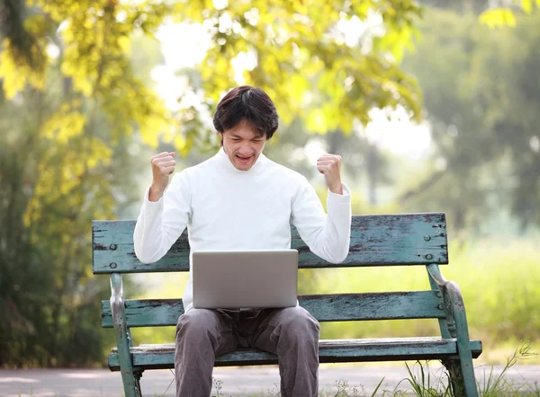 A young handsome man asian using laptop sitting on a bench in a — Stock Photo, Image