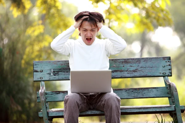 Un jeune bel homme asiatique en utilisant un ordinateur portable assis sur un banc dans un — Photo