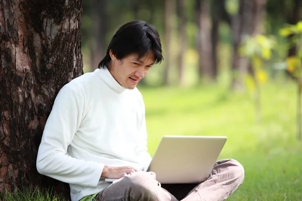 Un tânăr îşi foloseşte laptopul pe iarbă — Fotografie, imagine de stoc